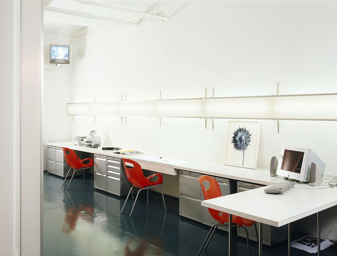 weiße Arbeitstische und rote Schalenstühle in einem Büro
