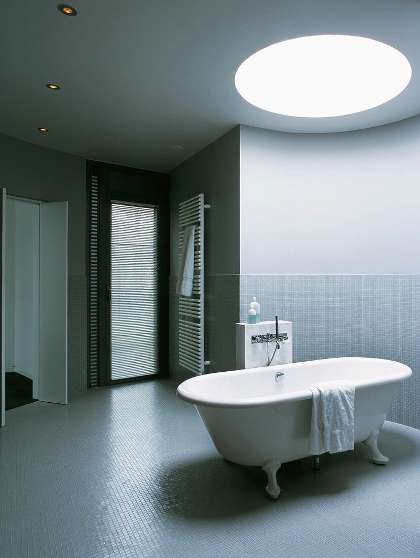 Eine freistehende Badewanne unter runder Deckenöffnung eines Badezimmers mit Glasbausteinen
