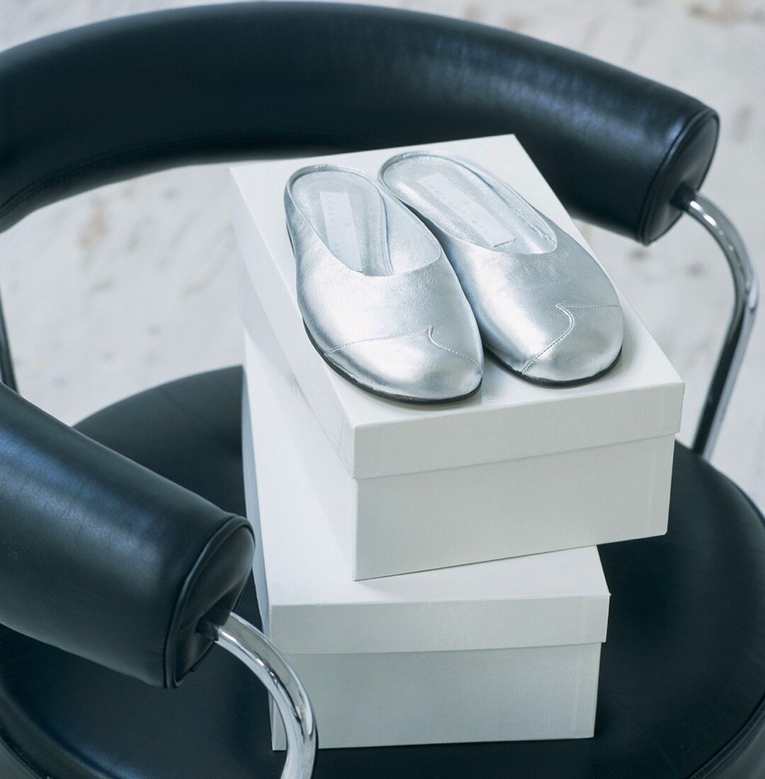 Silberne Hausschuhe und weiße Schuhkartons auf schwarzen Lederstuhl