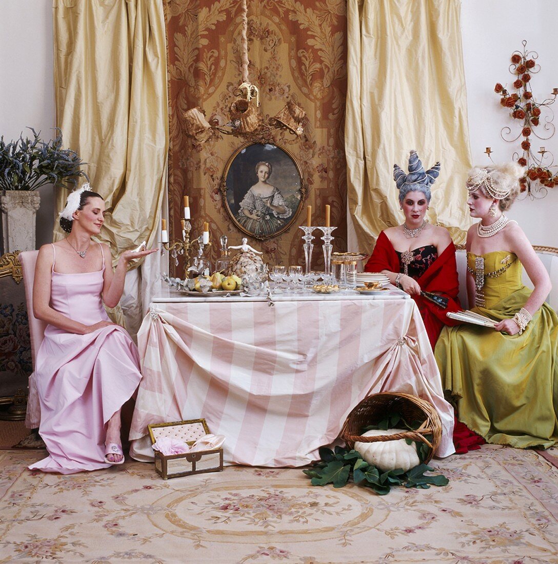 Three women in Baroque clothing sitting around dining table