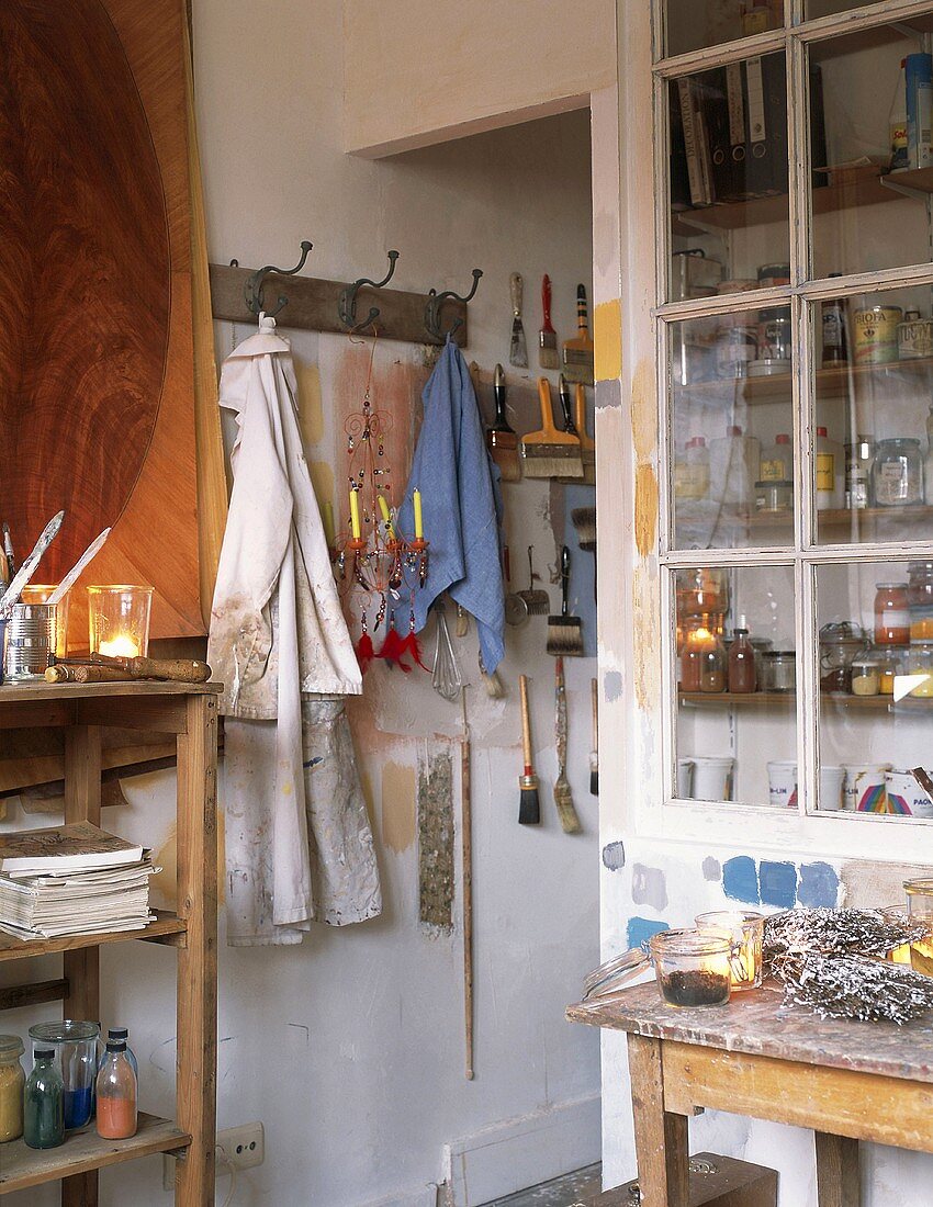 Atelier mit Vitrinenschrank, einfachem Holzregal und vielen Malutensilien