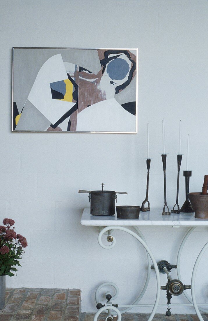 Modernes Wandbild mit Metallrahmen; darunter ein weisser Tisch mit geschwungenen Tischbeinen