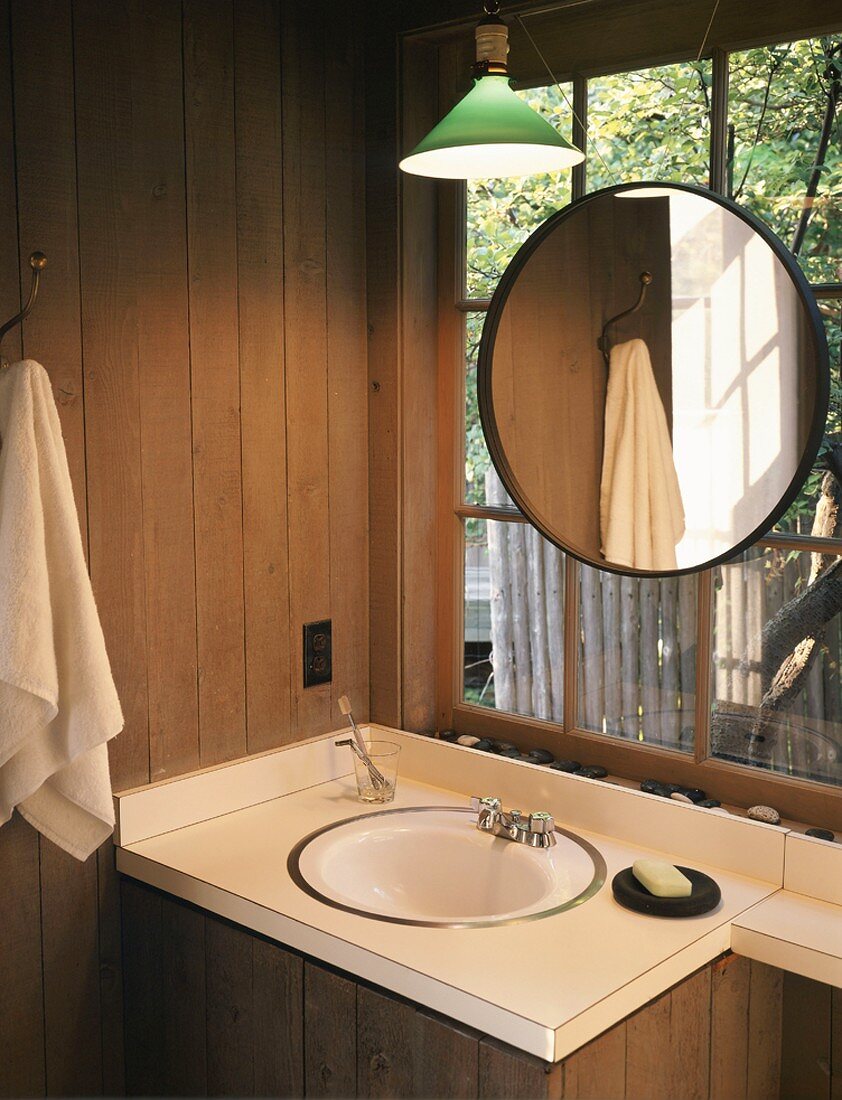 Washstand with basin below round mirror hung on lattice window