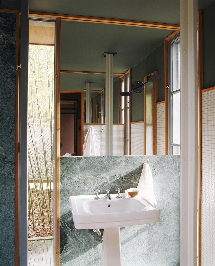 Pedestal sink below large mirror on marble-clad wall