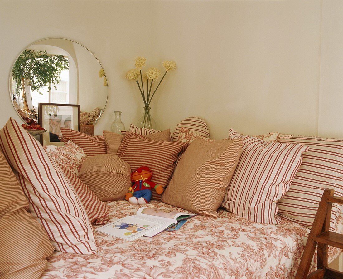 Patterns of white and red on comfortable sofa with many scatter cushions below round mirror on wall