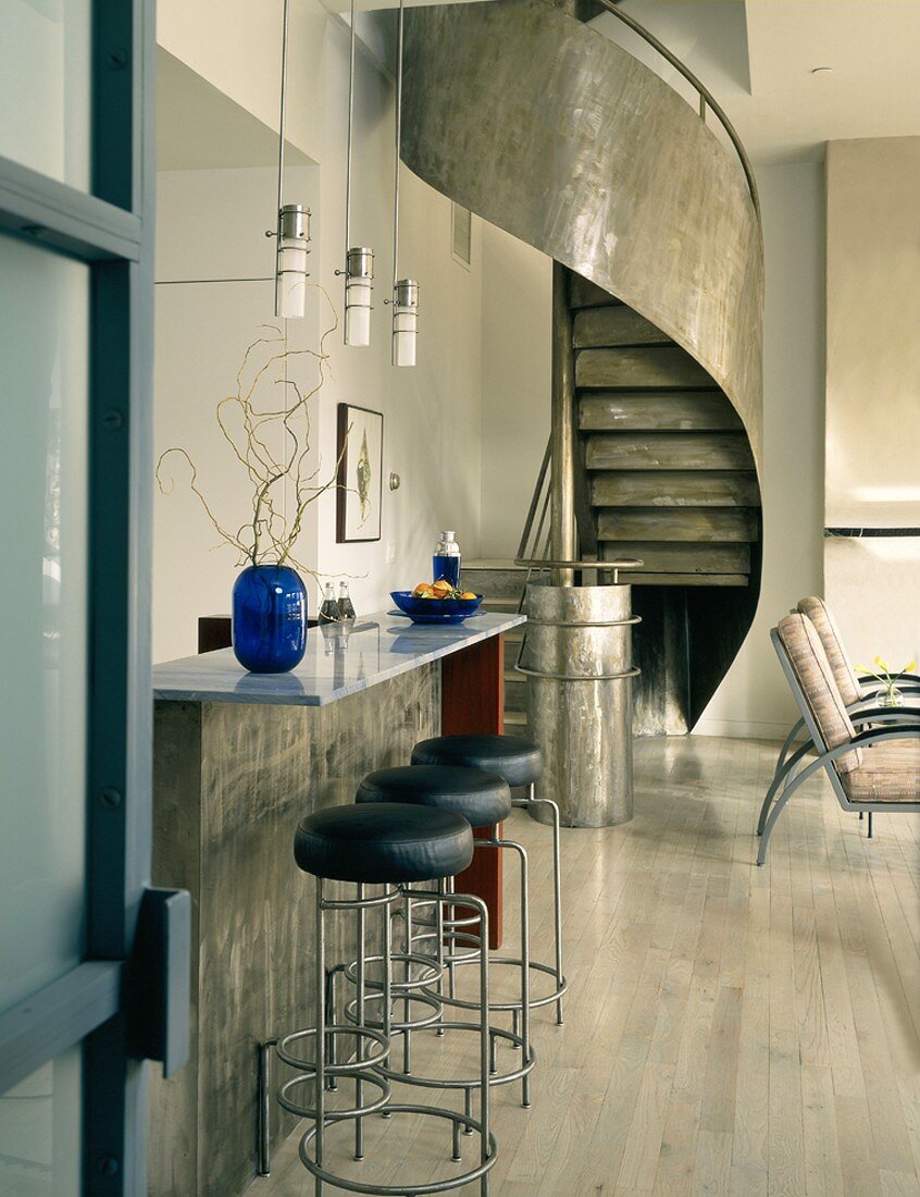 Modern, metal spiral staircase behind breakfast bar in open-plan interior