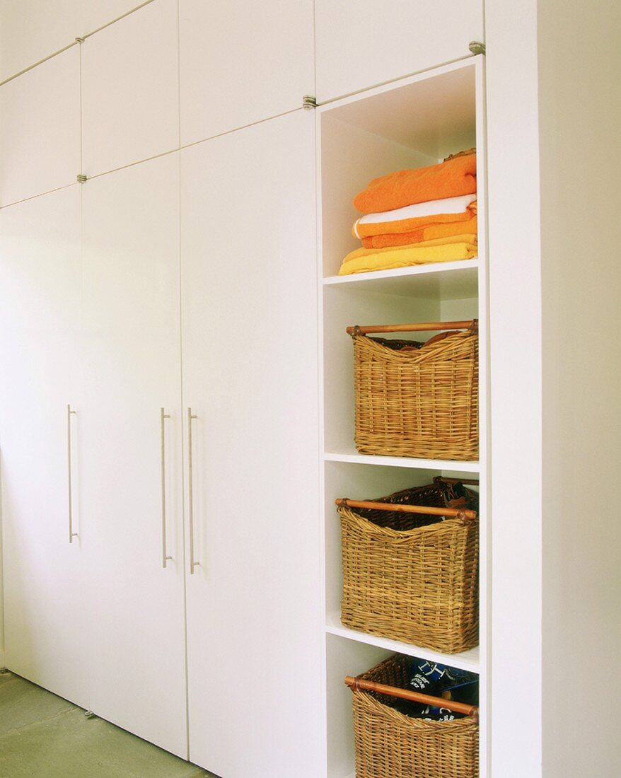 White fitted cupboards and open-fronted shelves of storage baskets