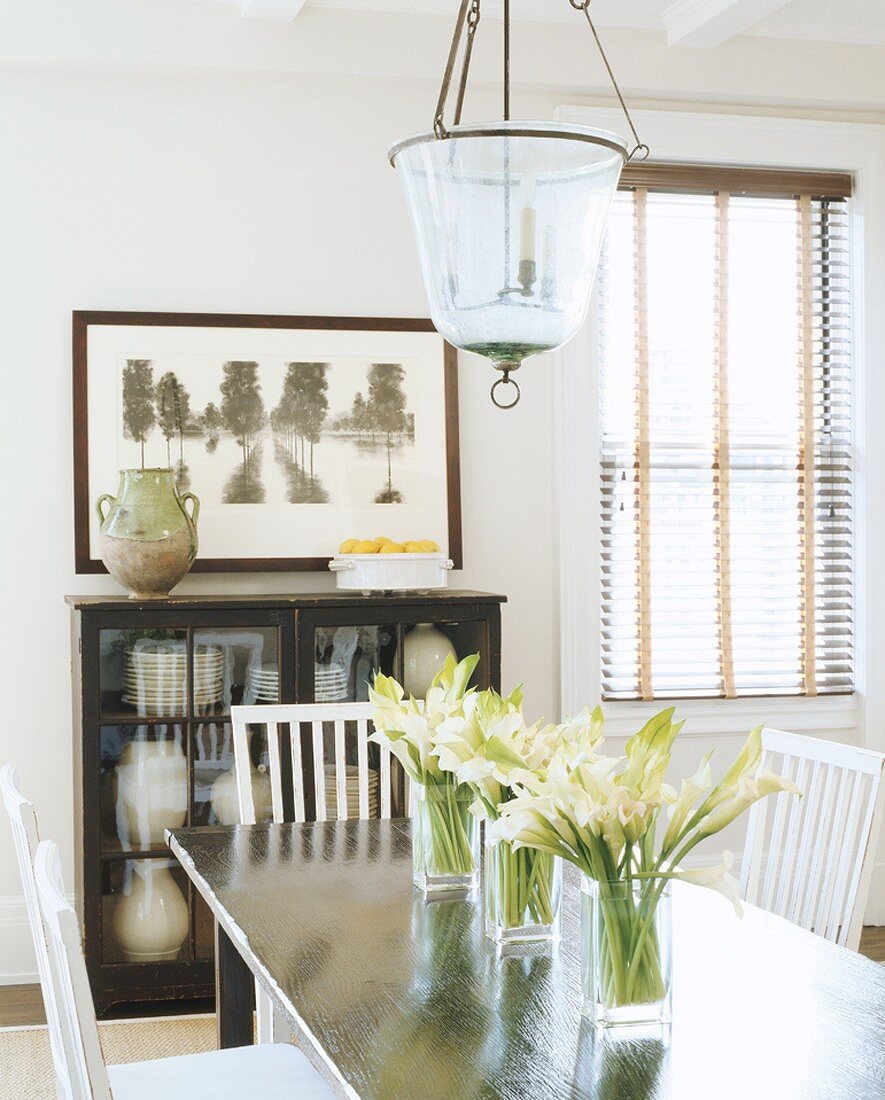 weiße Blumen in drei Glasvasen auf einem glänzenden Esstisch
