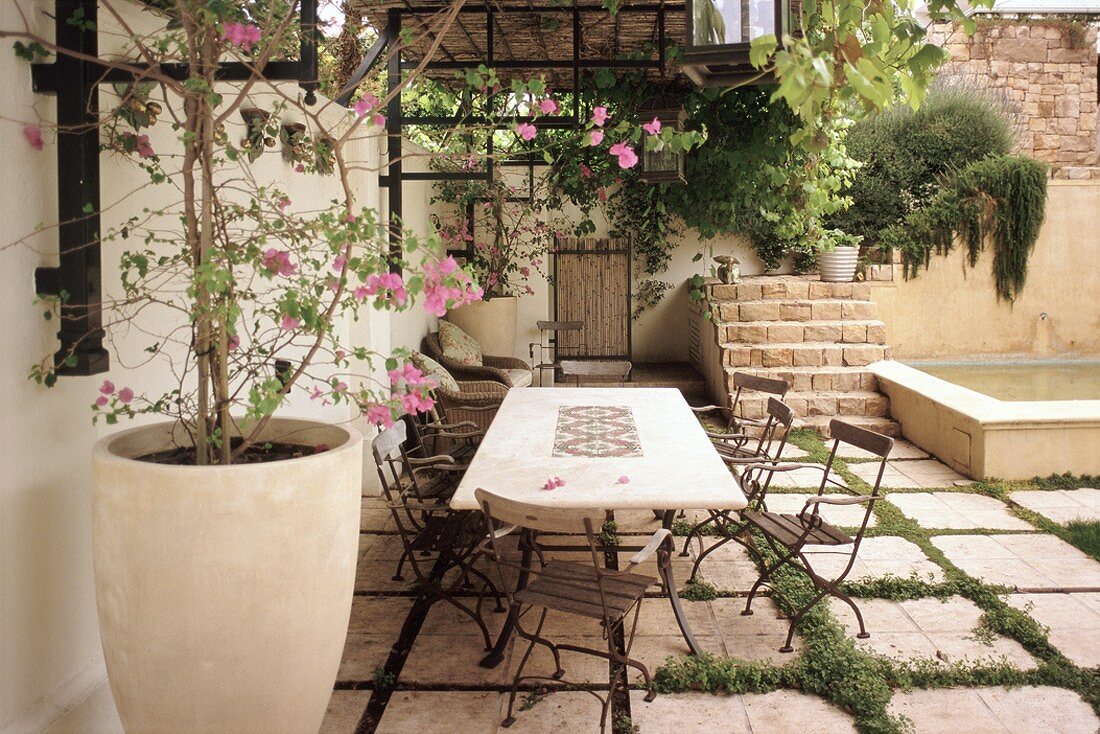 Geflieste Gartenterrasse mit Gartenmöbeln und einer großen, bepflanzten Bodenvase aus Terrakotta