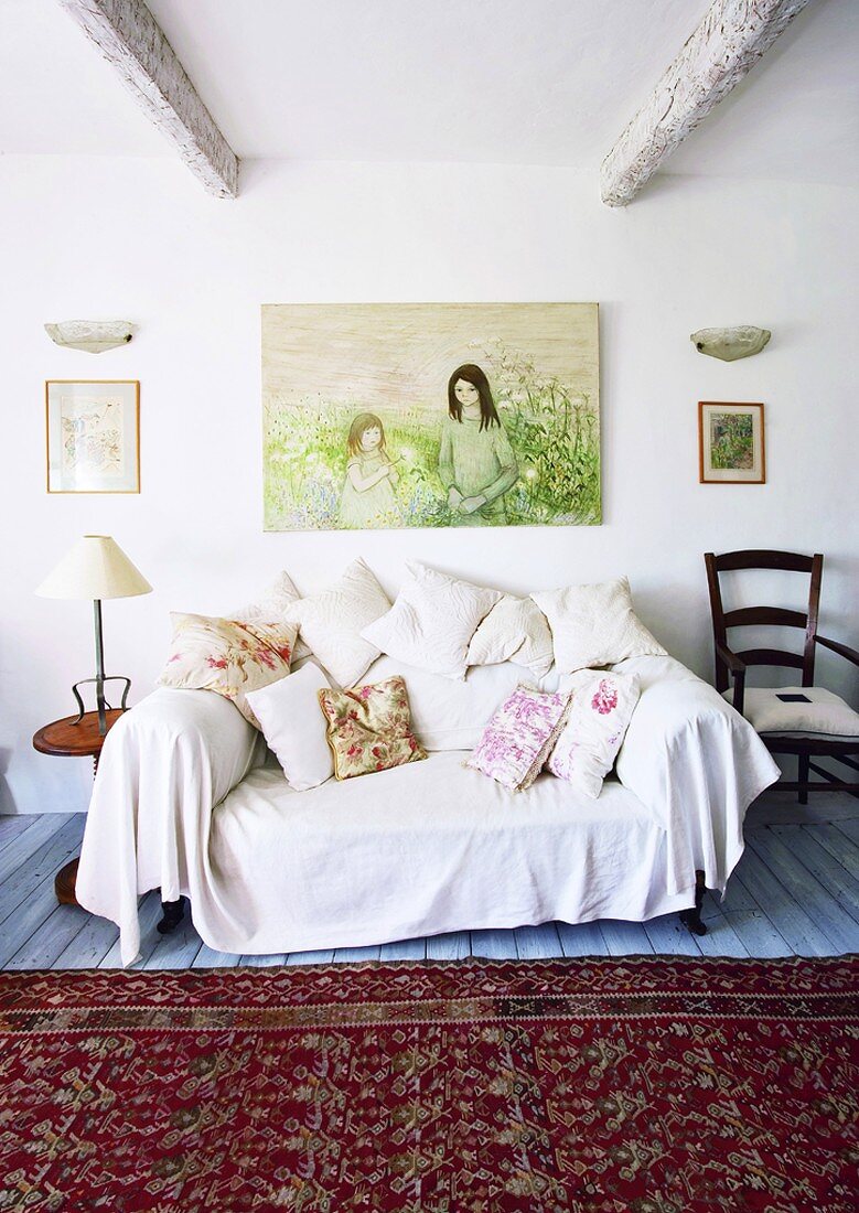 Couch mit großzügigem Überwurf und vielen Kissen; darüber ein modernes Gemälde
