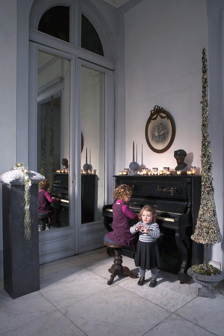 Zwei Mädchen an einem antiken Klavier in einem weihnachtlich geschmückten Raum