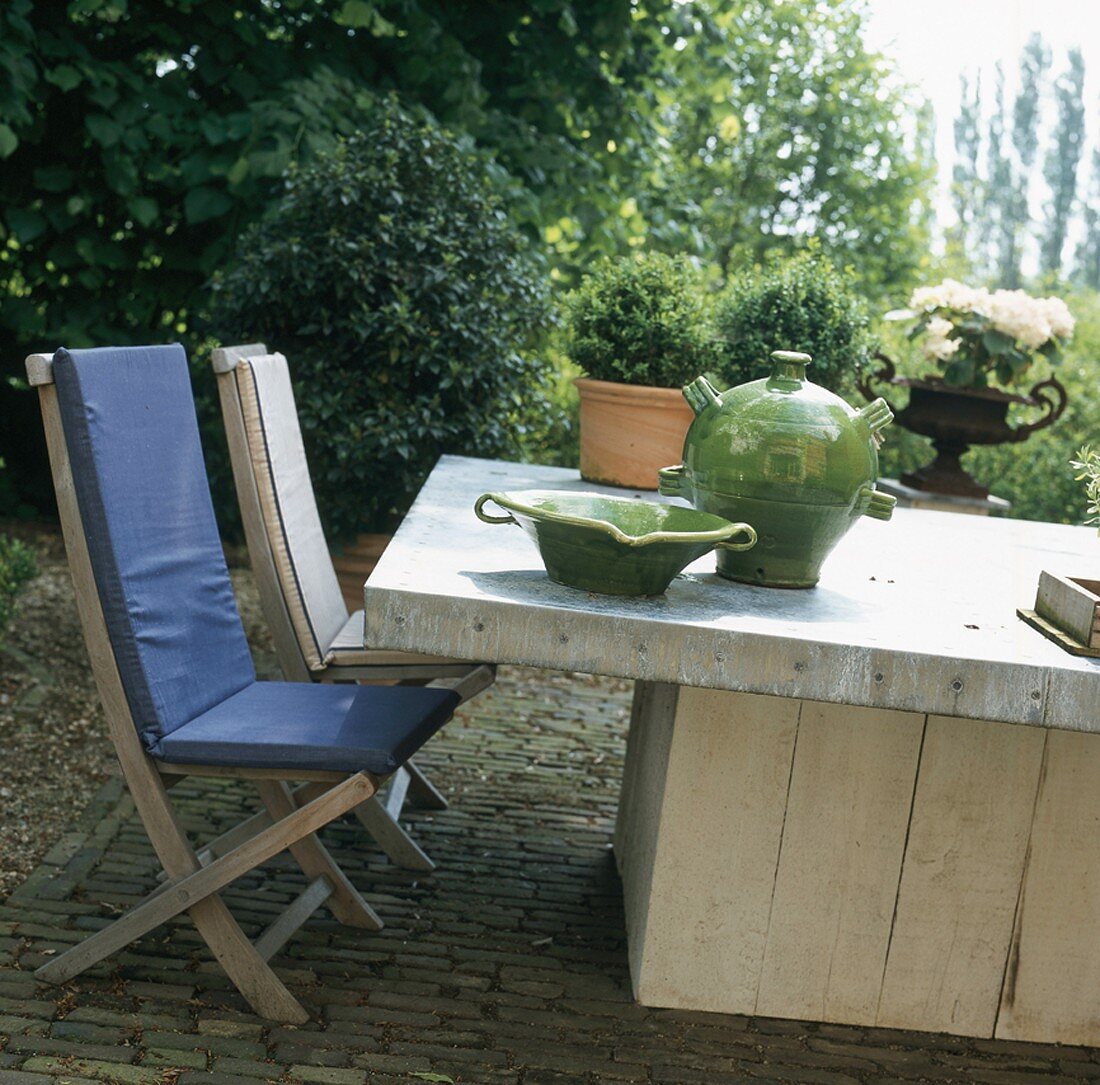 Wooden furniture on cobbled terrace with plants in background