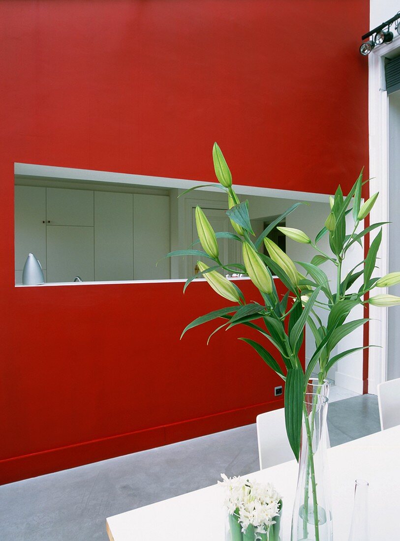 In einer roten Wand eingeschnittene Küchentheke; davor ein Esstisch mit frischer Blumendekoration