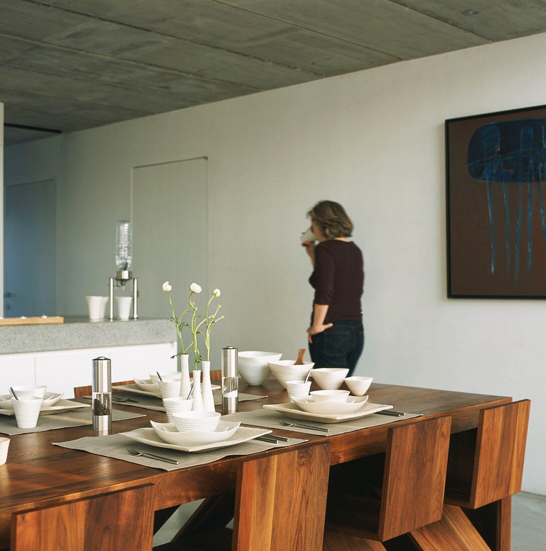 Woman drinking coffee in kitchen-dining room with set dining table in foreground