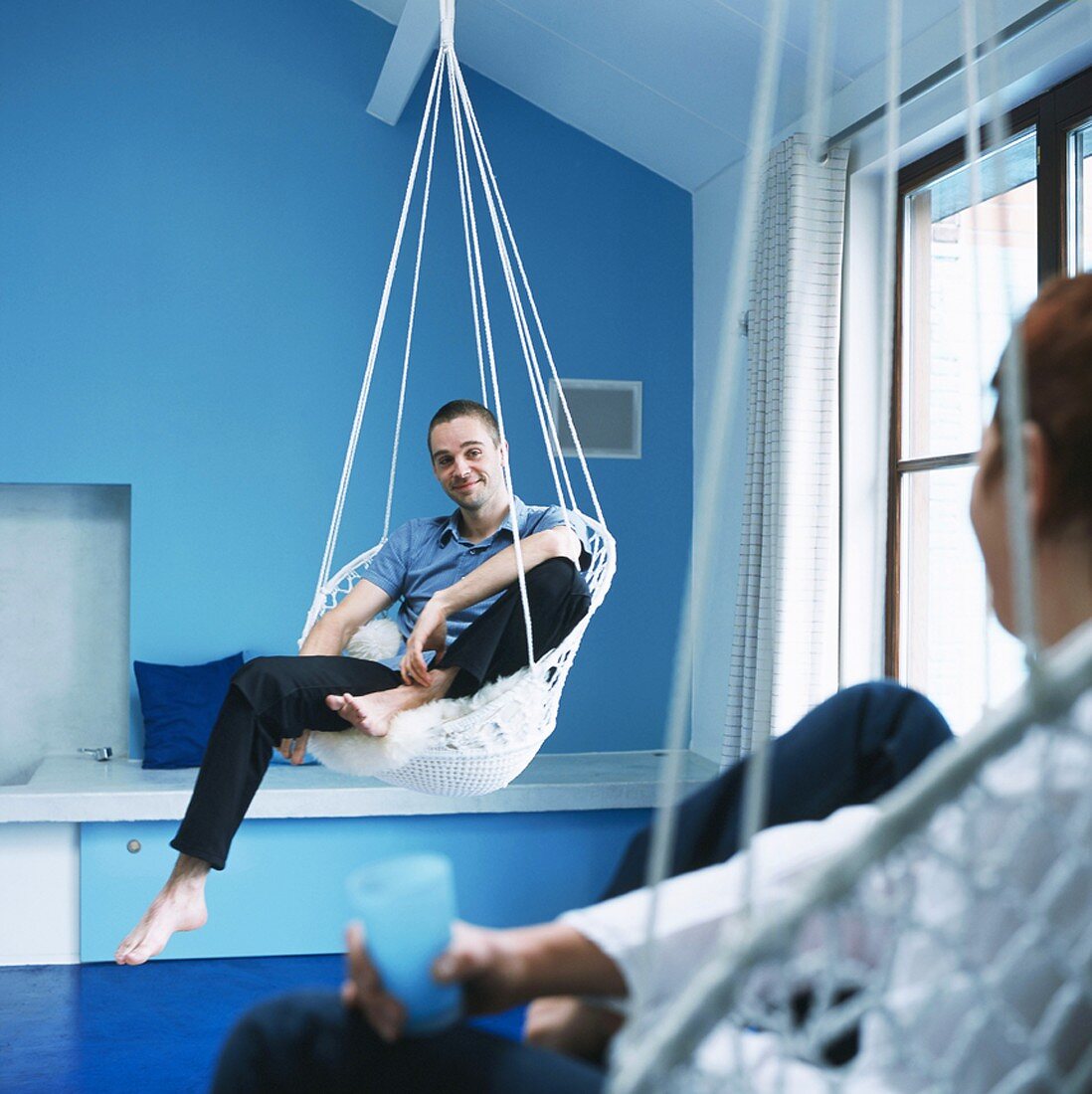 Two men sitting in hanging chairs in blue bedroom