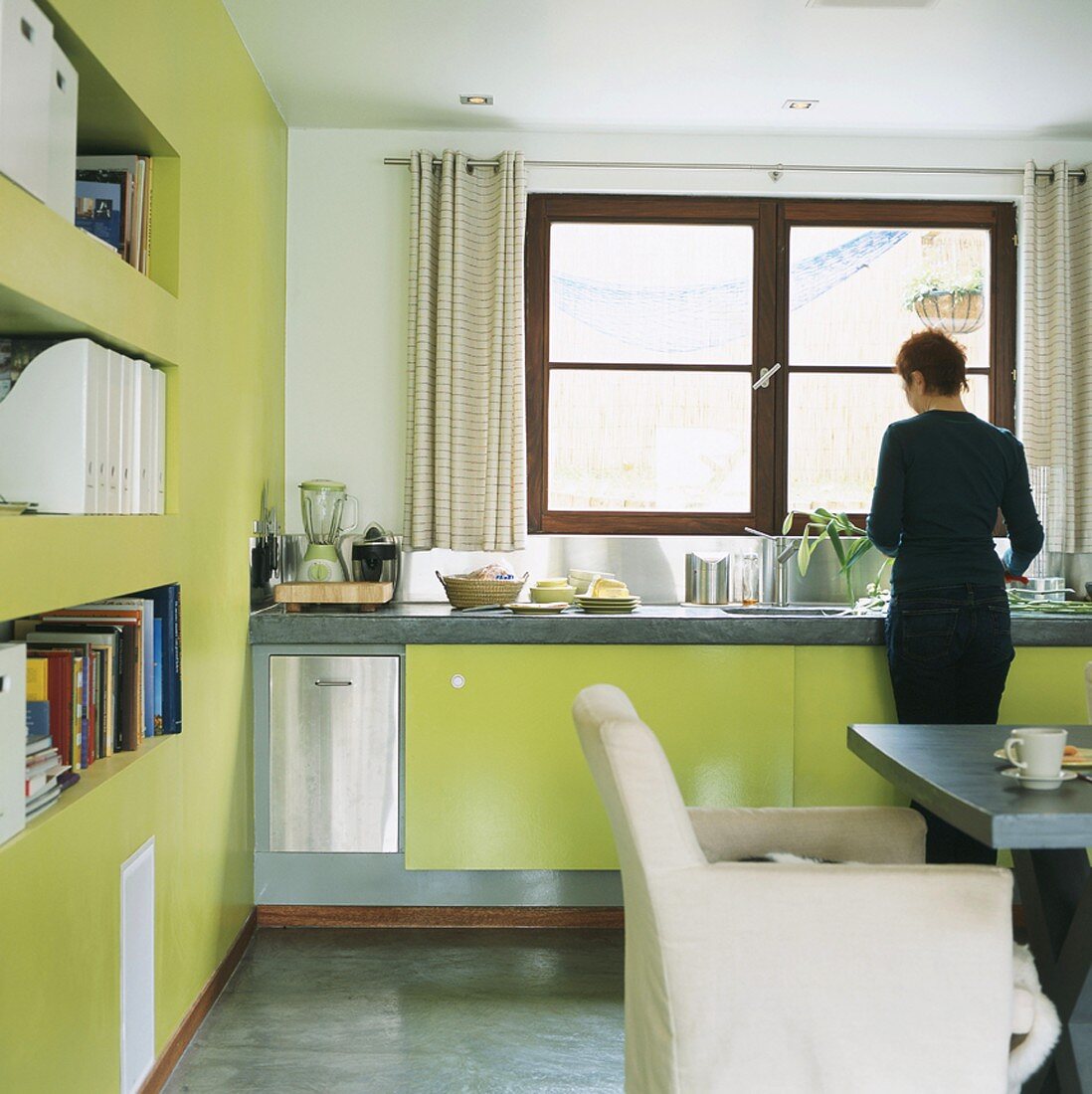 Woman washing up in kitchen with green units