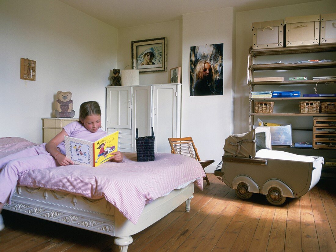 Mädchen liegt auf dem Bett im Kinderzimmer & liest Kinderbuch