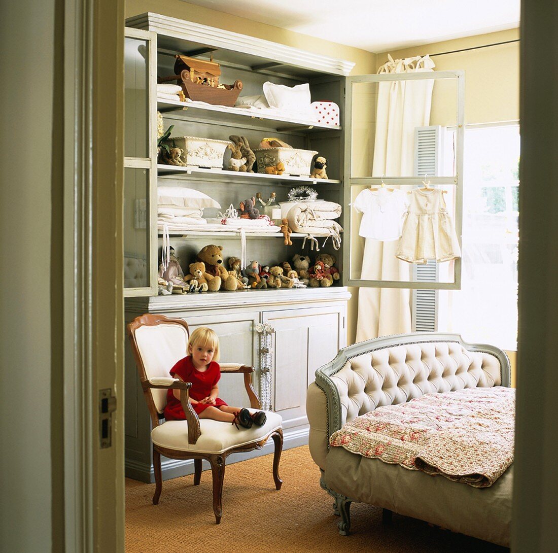 Little girl sitting on chair in front of cupboard in child's bedroom