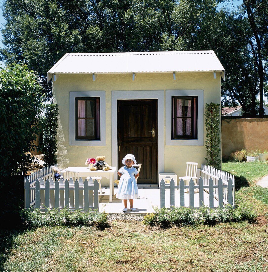 Kleines Mädchen vor Gartenhaus mit Gartenzaun