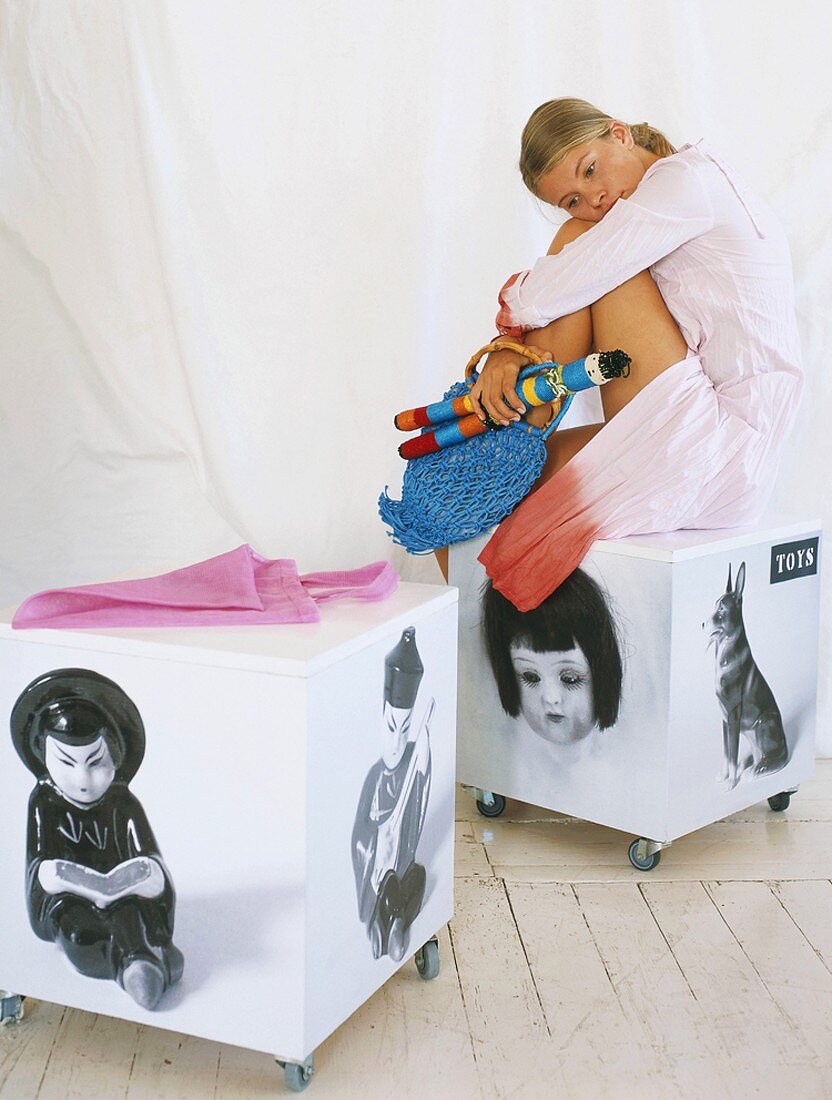 Mädchen sitzt auf einer Spielzeug-Box mit Rollen