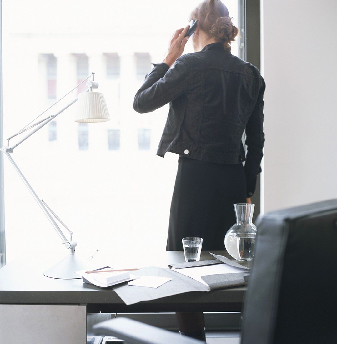 Frau steht am Bürofenster und telefoniert