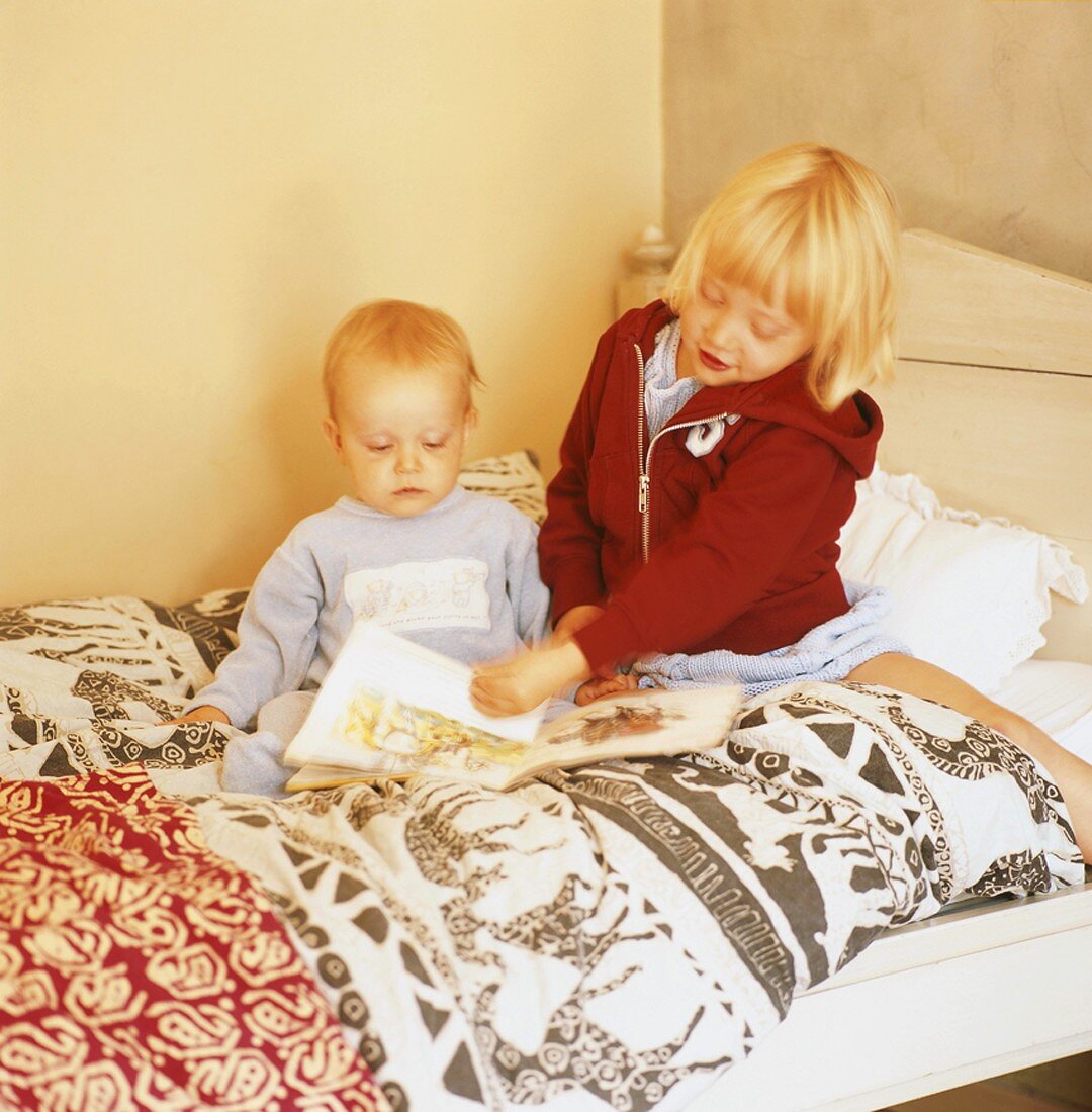 Zwei Kinder sitzen auf dem Bett und blättern im Bilderbuch