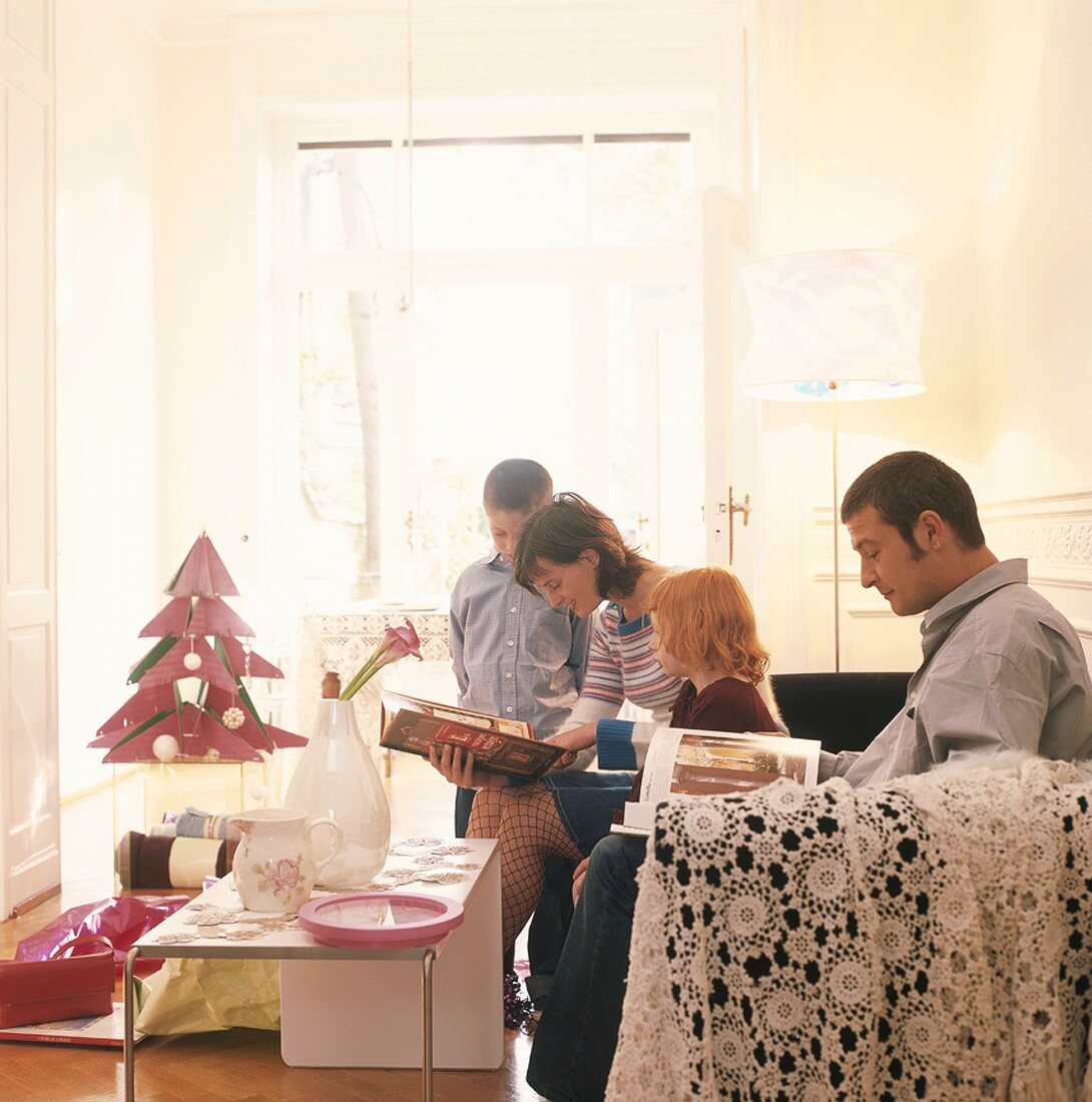 Familie blättert in Büchern im Wohnzimmer zu Weihnachten
