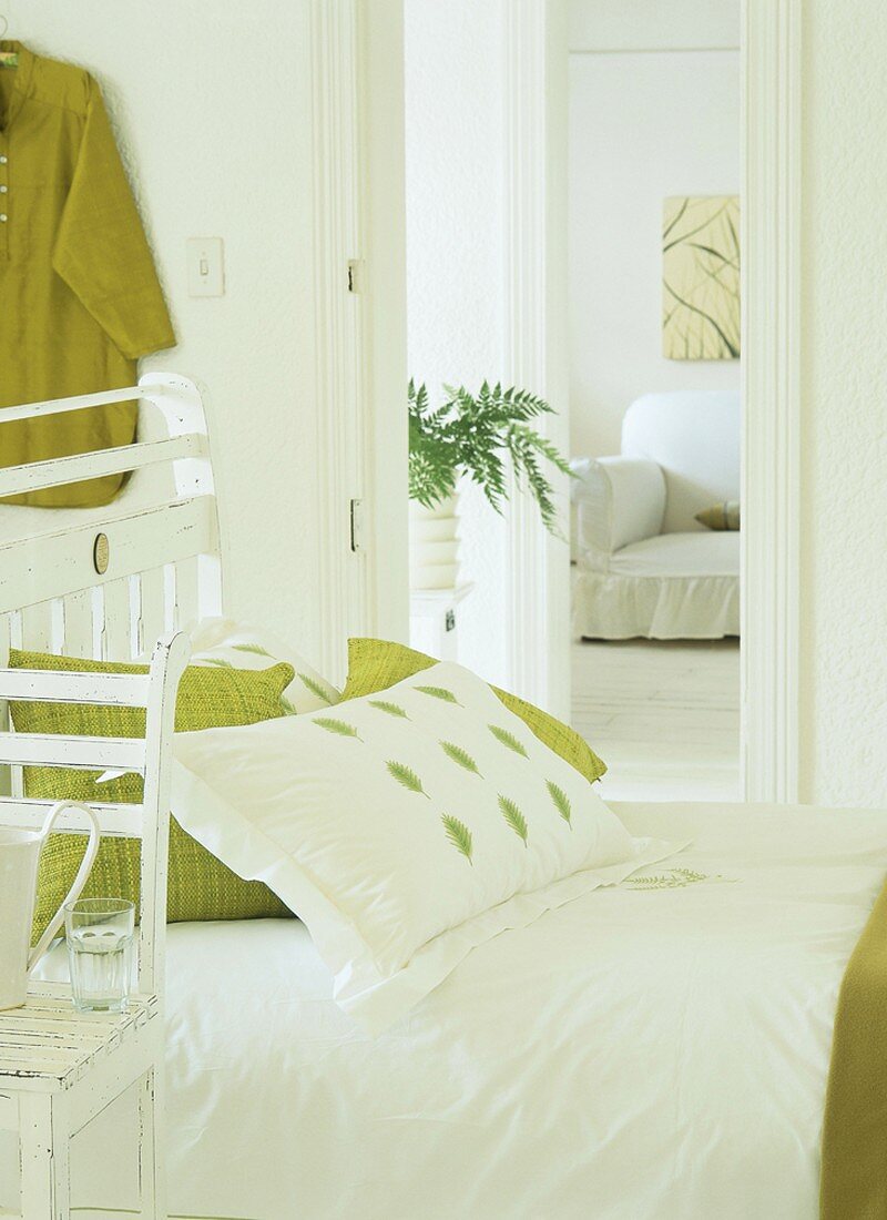 Gemütliches Holzbett im Shabby Chic Stil, gemixt mit frischen Grüntönen, dahinter eine weiße Couch