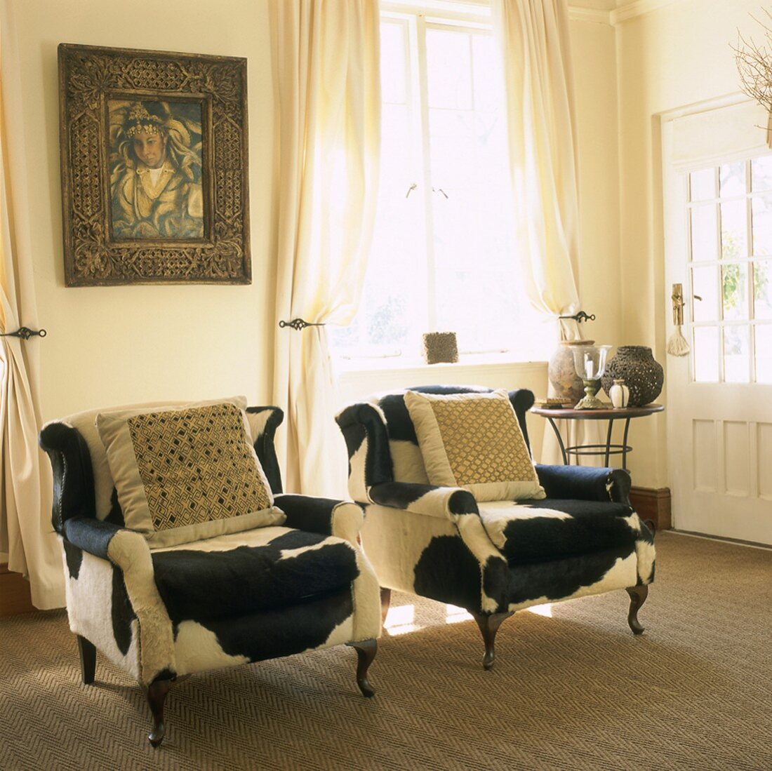 Zwei mit Kuhfell überzogene, antike Sessel und ein Gemälde in einem hellen Wohnraum
