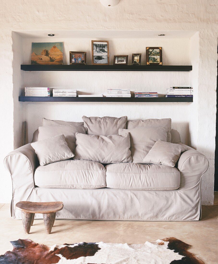 Gemütliche Couch in einer Nische, darüber zwei einfache Wandregale