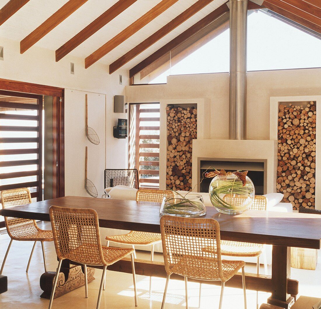 Großer Esstisch und Kamin in einem Raum mit schräger Holzbalkendecke und verglastem Giebel