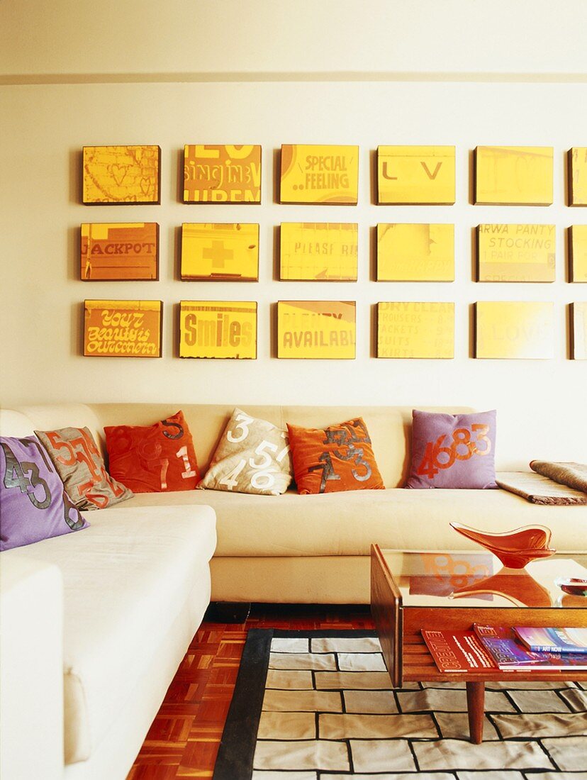 Ecksofa mit bunten Kissen, an der Wand eine gelbe Bilderserie