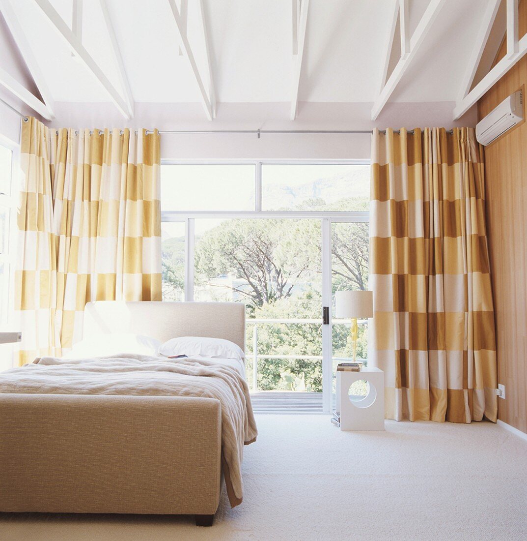 Schlafzimmer in Brauntönen mit verglaster Front und weisser Holzbalkendecke