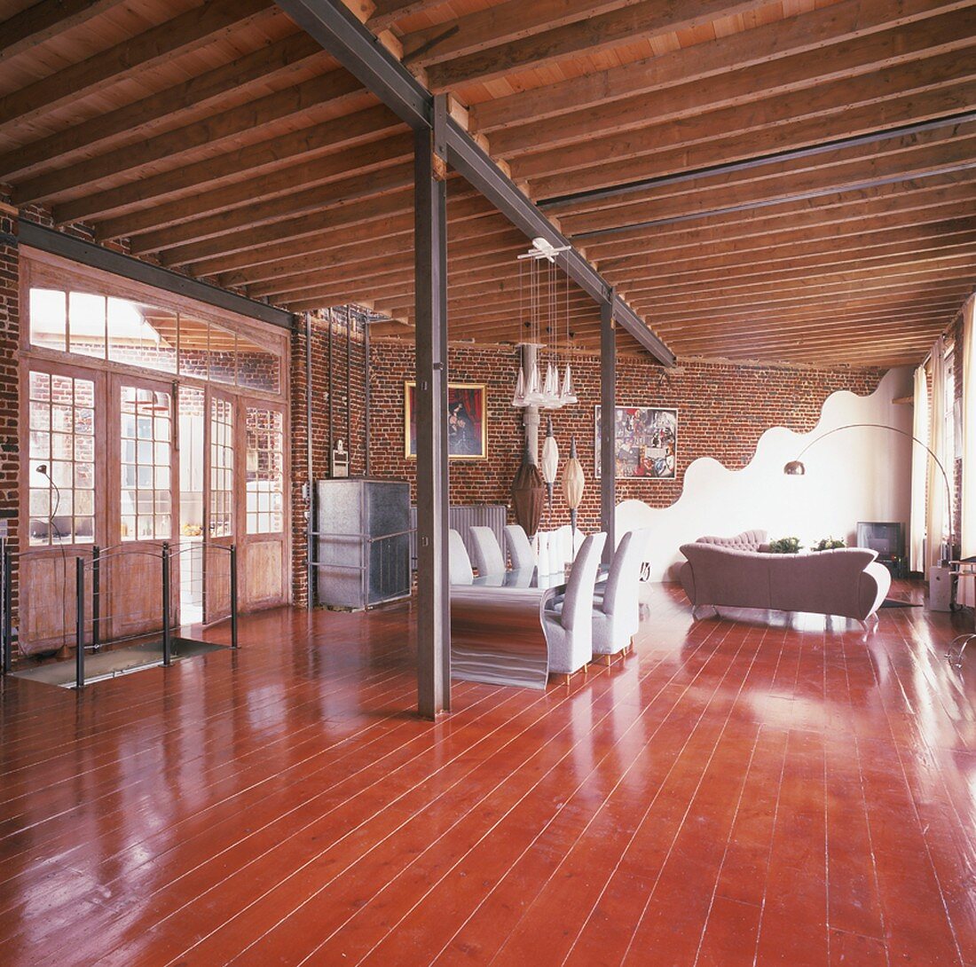 Designermöbel in einem Loft mit Holzbalkendecke, Stahlträgern und Dielenboden aus Kirschholz