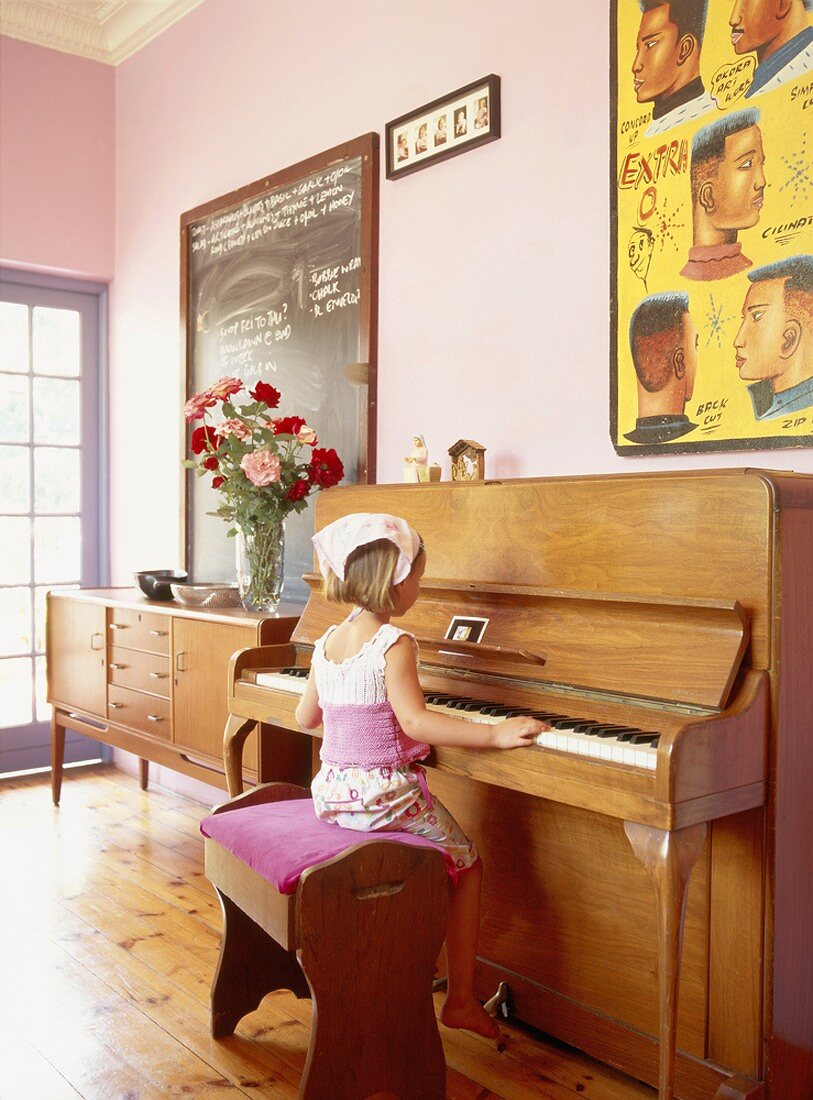 Ein Kind am Klavier in einem Zimmer mit Stuckdecke und Dielenboden