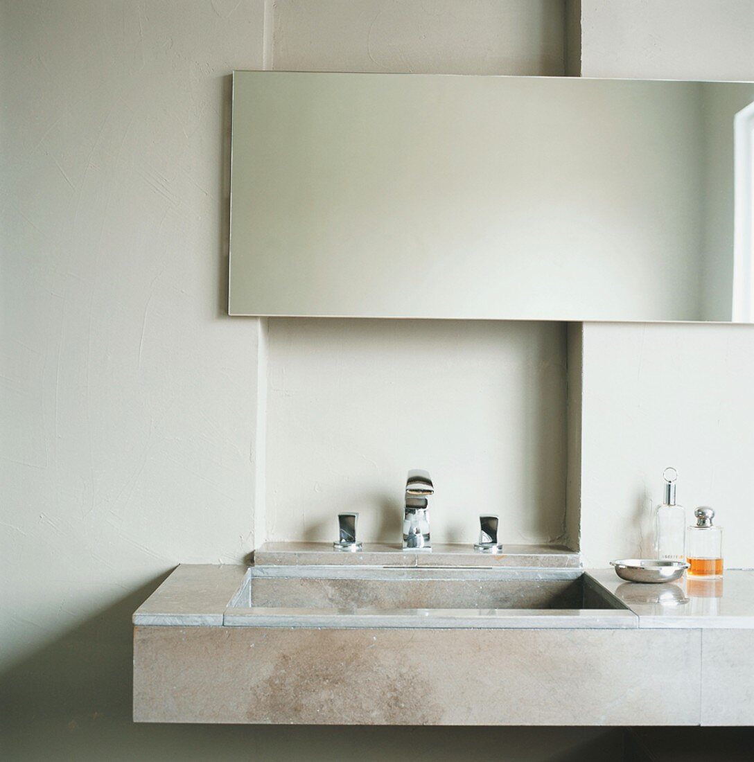 Ein Waschtisch aus Naturstein mit einfachem Badezimmerspiegel vor einer Wandnische