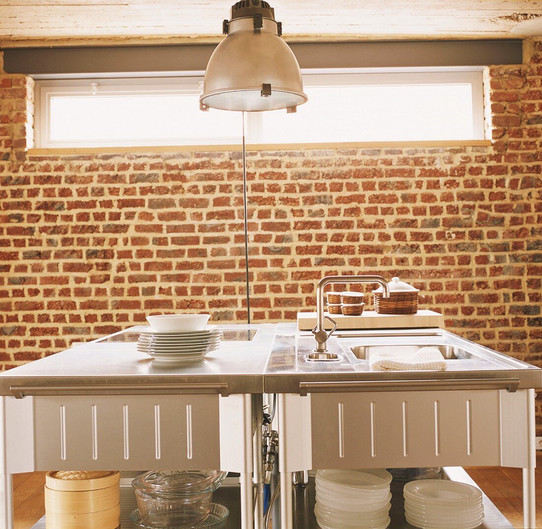 Ein Küchenblock mit Edelstahloberfläche vor einer Backsteinwand mit breitem Oberlicht