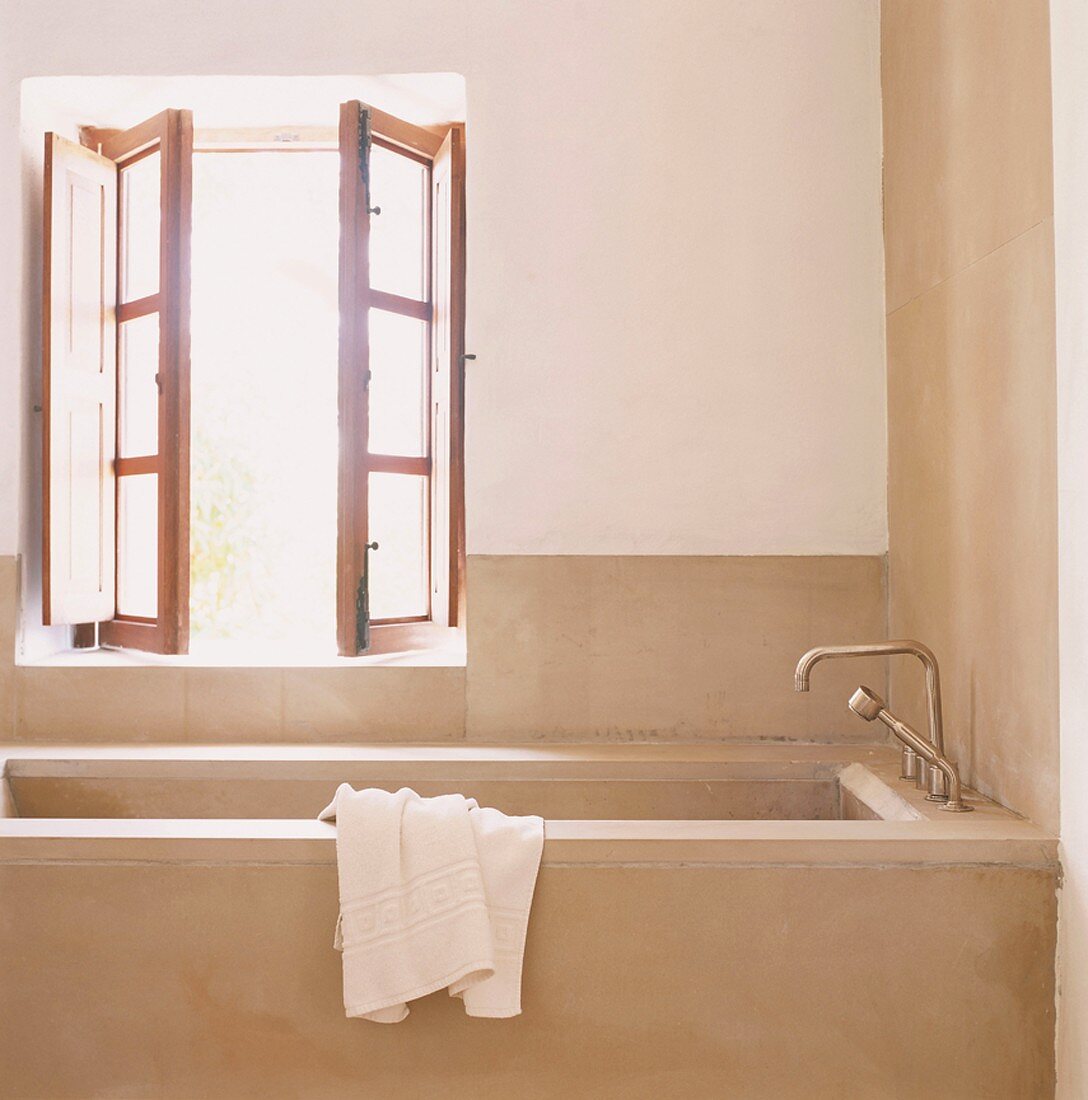 Eine Badewanne aus Natursteinplatten unter einem Holzdoppelfenster