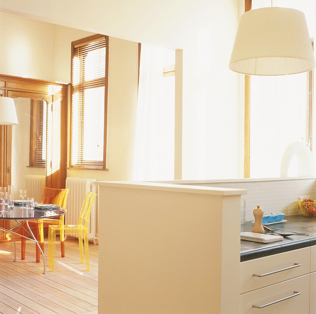 Ein heller Raum mit eleganter Küchentheke und bunten Plexiglasstühlen an einem Glastisch