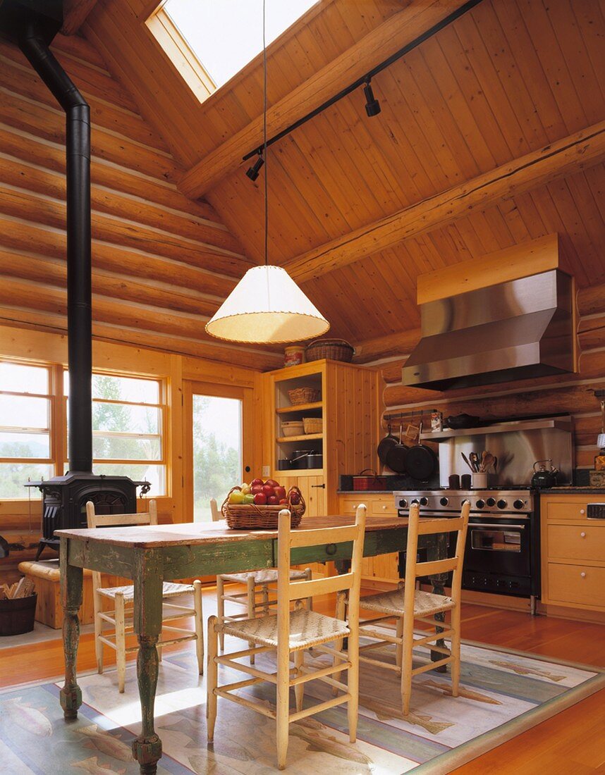 Der alte Bauerntisch und der Holzofen tragen zur warmen Atmosphäre in der Wohnküche des gemütlichen Holzhauses bei