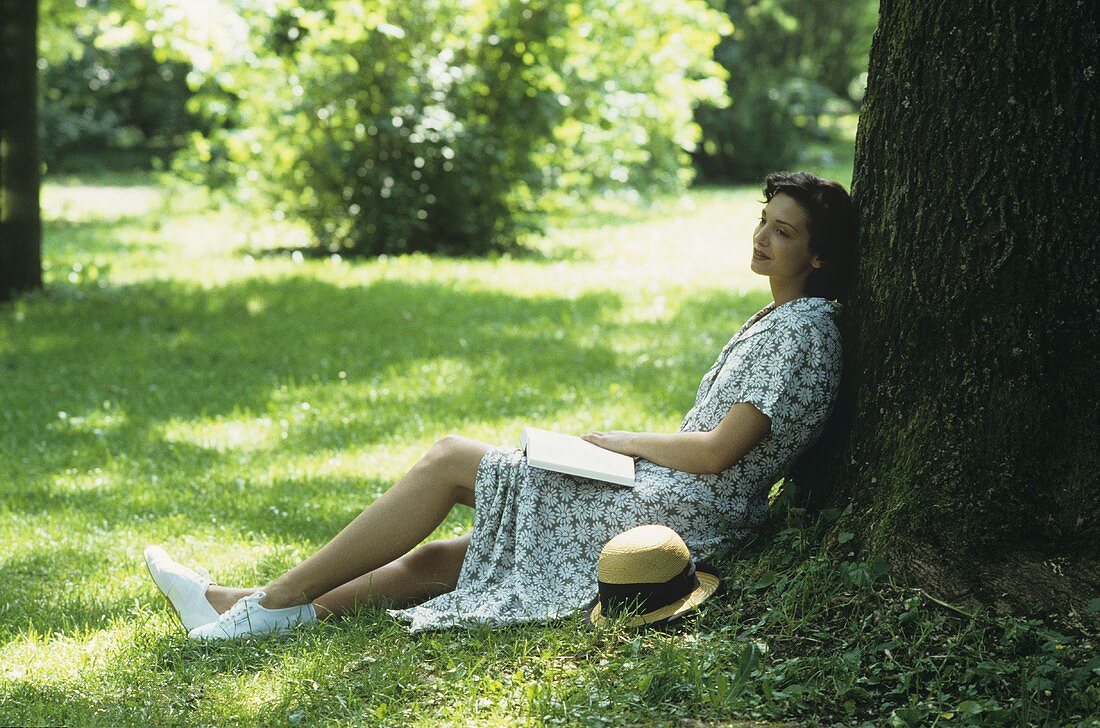 Woman sitting on grass leaning against a tree