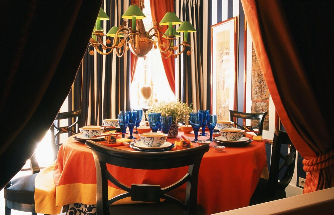Ein farbenfroh gedeckter Esstisch mit Bidermeierstühlen in einem schwarzweiss gestreiften Raum