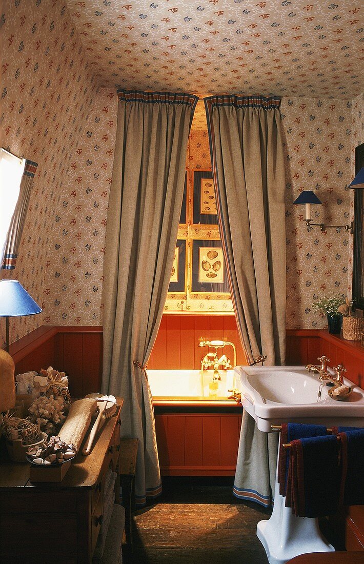 In dem 20er Jahre Badezimmer mit Holzvertäfelung und Blümchentapete ist die Badewanne durch einen Vorhang abgetrennt