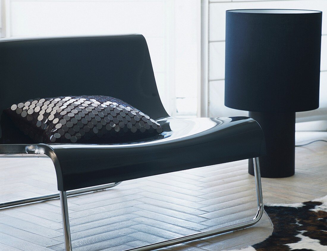 Schwarze Designermöbel mit einem Pailettenkissen in einem Raum mit hellem Fischgrätparkett