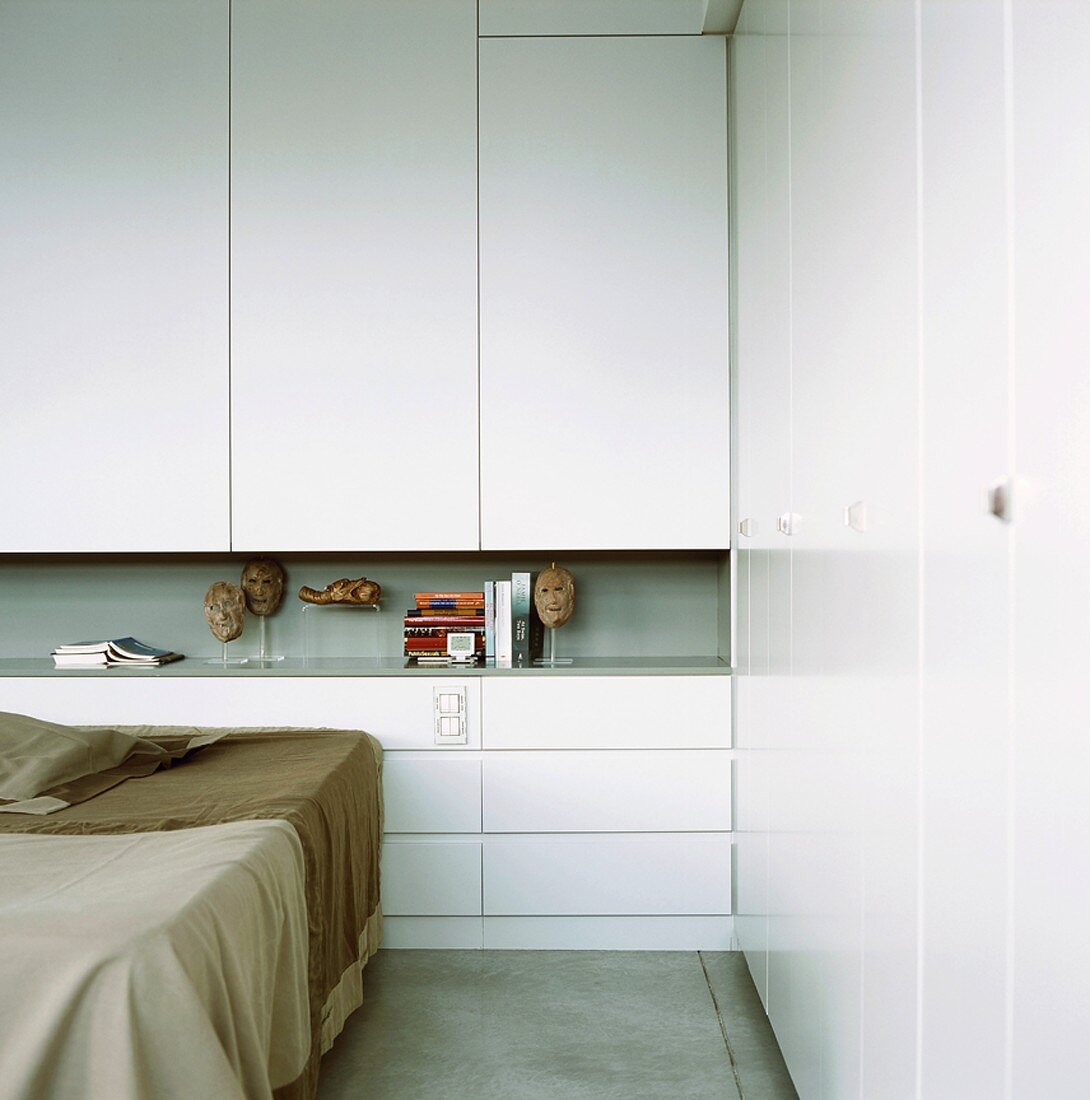 Eine Ecke eines Schlafzimmers mit weißem Einbauschrank und durchlaufender Wandnische als Ablagefläche