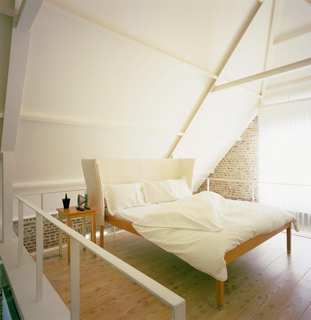 Dezente Schlafzimmereinrichtung im Dachgeschoss mit Backsteinwand und weiss verkleideter Dachschräge