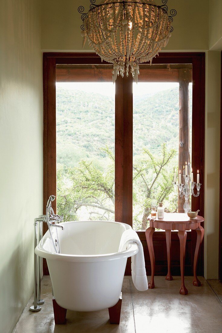 Ein prunkvoller Kronleuchter wertet das klassisch-schlichte Badezimmer mit freistehender Badewanne auf