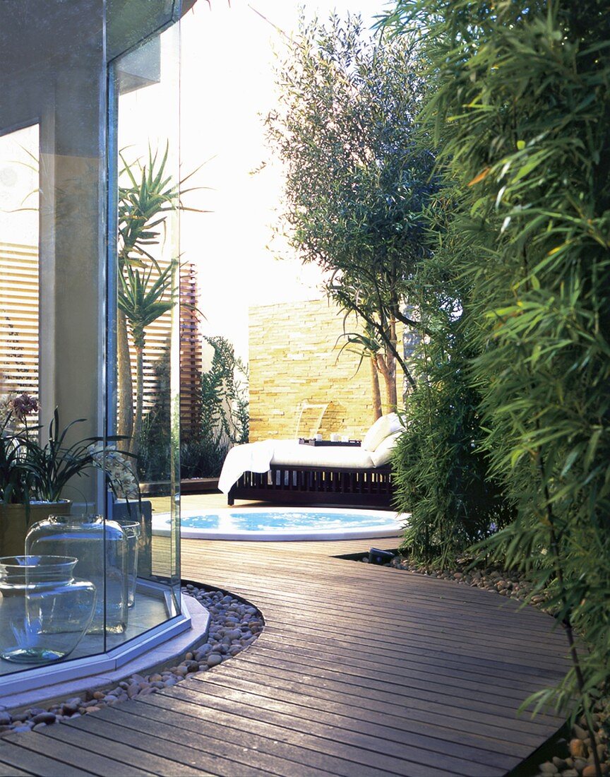 Ein Holzsteg führt zur modern gestalteten Terrasse mit Whirlpool und großer Sonnenliege