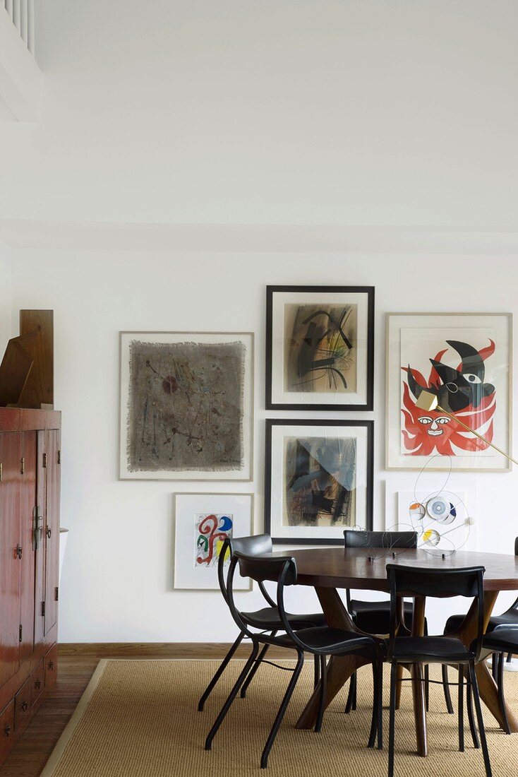Ein runder Esstisch mit Stühlen auf einem Sisalteppich vor einer Wand mit Kunstdrucken