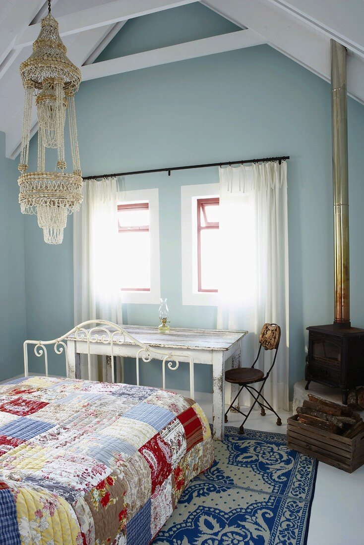 Ein freundliches Schlafzimmer im Stilmix mit orienatlischer Hängeleuchte, antikem Holzofen und weißem Metallbett